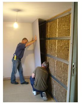 two men installing a studio wall system by fixing acoustic plasterboard to resilient bars on stud frame